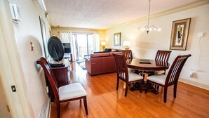 A dining area with a wooden table and chairs, a sofa, and a television in the background. - Lake & Golf Views in Saddlebrook Resort. 2 bed/2bath (Wesley Chapel)