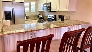 A kitchen with white cabinets, a granite countertop, a stainless steel refrigerator, a microwave, a stove, and two wooden bar stools. - Lake & Golf Views in Saddlebrook Resort. 2 bed/2bath (Wesley Chapel)