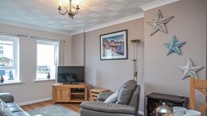 A living room with a sofa, a television on a wooden stand, a fireplace, and decorative star wall art.