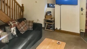 A living room with a black sofa, plaid cushions, a wooden coffee table, a television on the wall, and a bookshelf. - 2 bedroom accommodation in Melmerby (Melmerby)