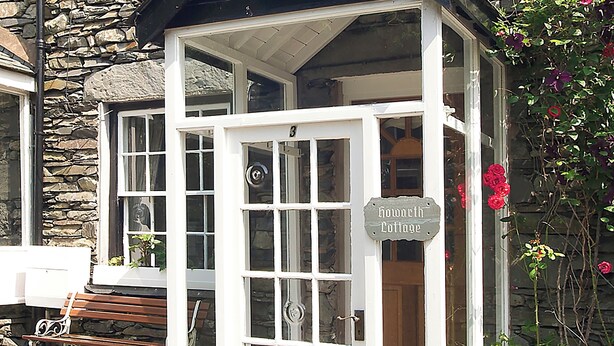 A stone building with a white cottage-style entrance, a bench outside, and a sign reading "Howarth Cottage." - 2 bedroom accommodation in Troutbeck Bridge (Troutbeck Bridge)