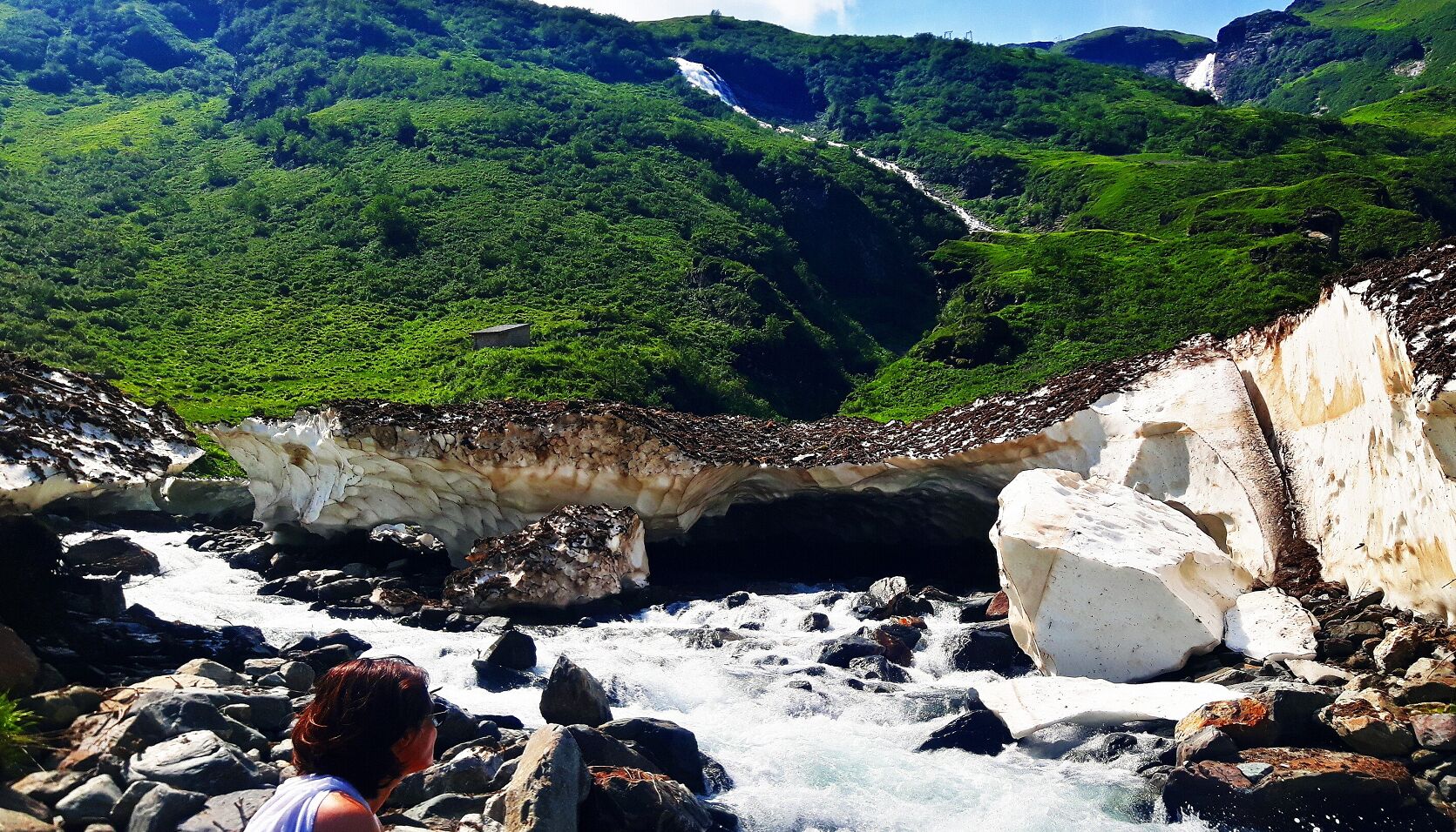 Eine felsige Landschaft mit einem Wasserfall und einer Person im Vordergrund.