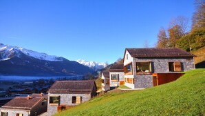 A hillside with a stone house featuring large windows and a sloped roof, overlooking a valley and snow-capped mountains. - Delicious dining with a view of Hohe Tauern National Park,close to the ski lift (Bramberg am Wildkogel)