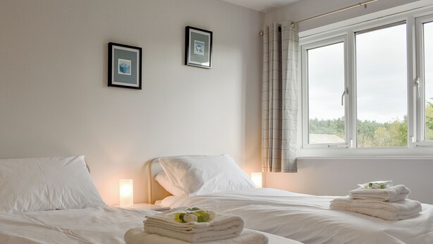 Une chambre d’hôtel avec deux lits, chacun équipé de draps et de serviettes blancs, une table de chevet avec une lampe et une fenêtre avec des rideaux.