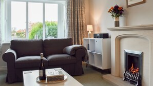 Un salon comprenant un canapé, une table basse avec une bouteille et une boîte, une cheminée et une fenêtre avec des rideaux.