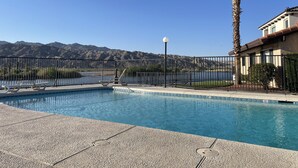 A swimming pool with a view of mountains, a palm tree, and a building with a tiled roof. - Condo in a Riverfront Complex (Bullhead City)
