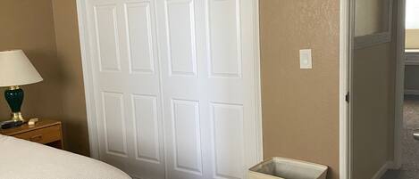 A bedroom with a bed, a nightstand, a lamp, a ceiling fan, a door, and a laundry basket.