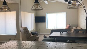 A dining area with a high ceiling, a ceiling fan, and pendant lights. There is a dining table with chairs, a window with blinds, and a television mounted on the wall. - Condo in a Riverfront Complex (Bullhead City)