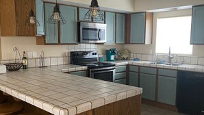 A modern kitchen with a large island, wooden cabinets, and pendant lighting. - Condo in a Riverfront Complex (Bullhead City)