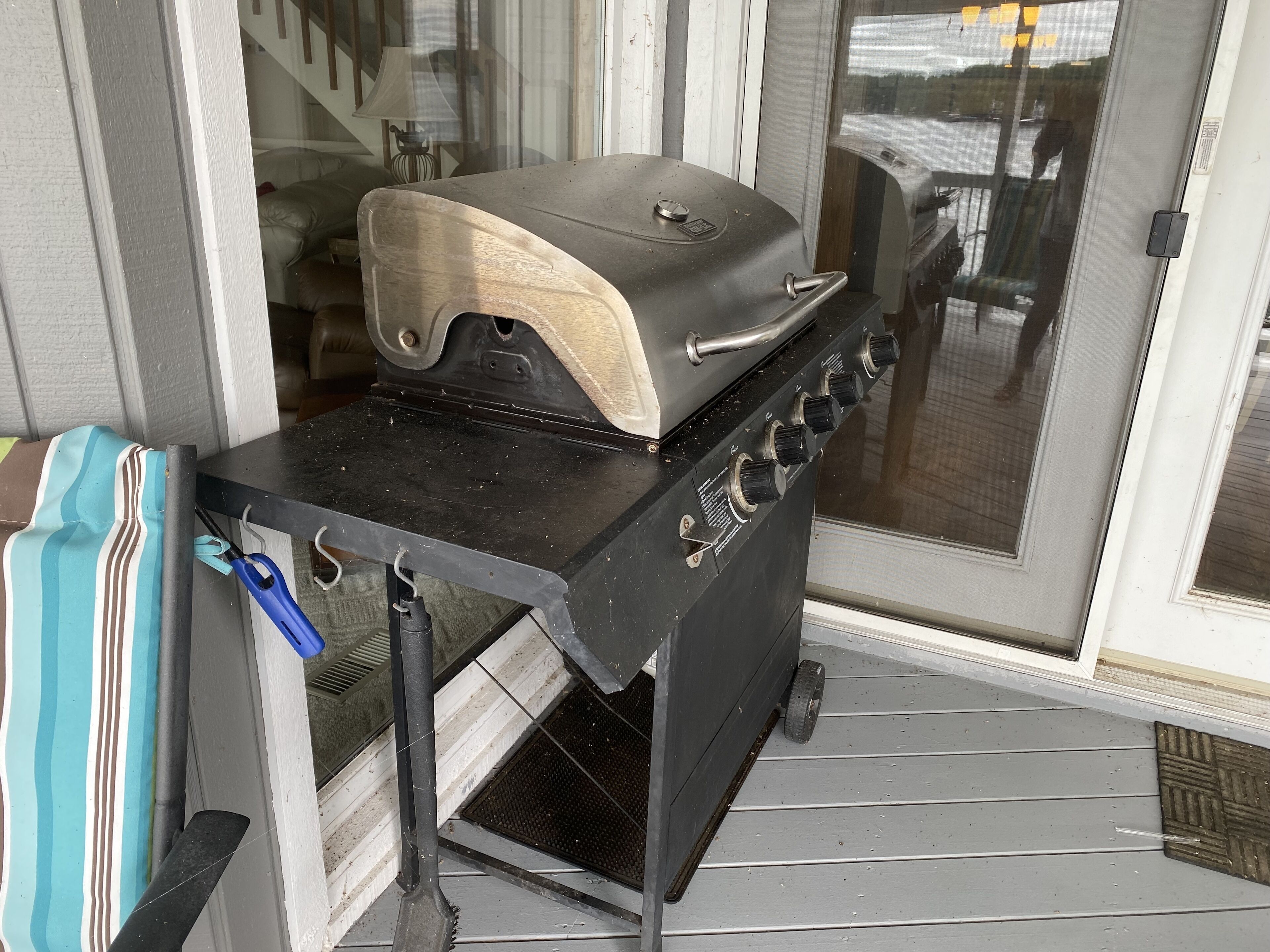 A portable grill on a porch with a sliding glass door in the background.