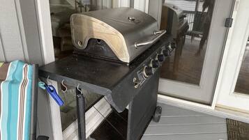 A portable grill on a porch with a sliding glass door in the background.
