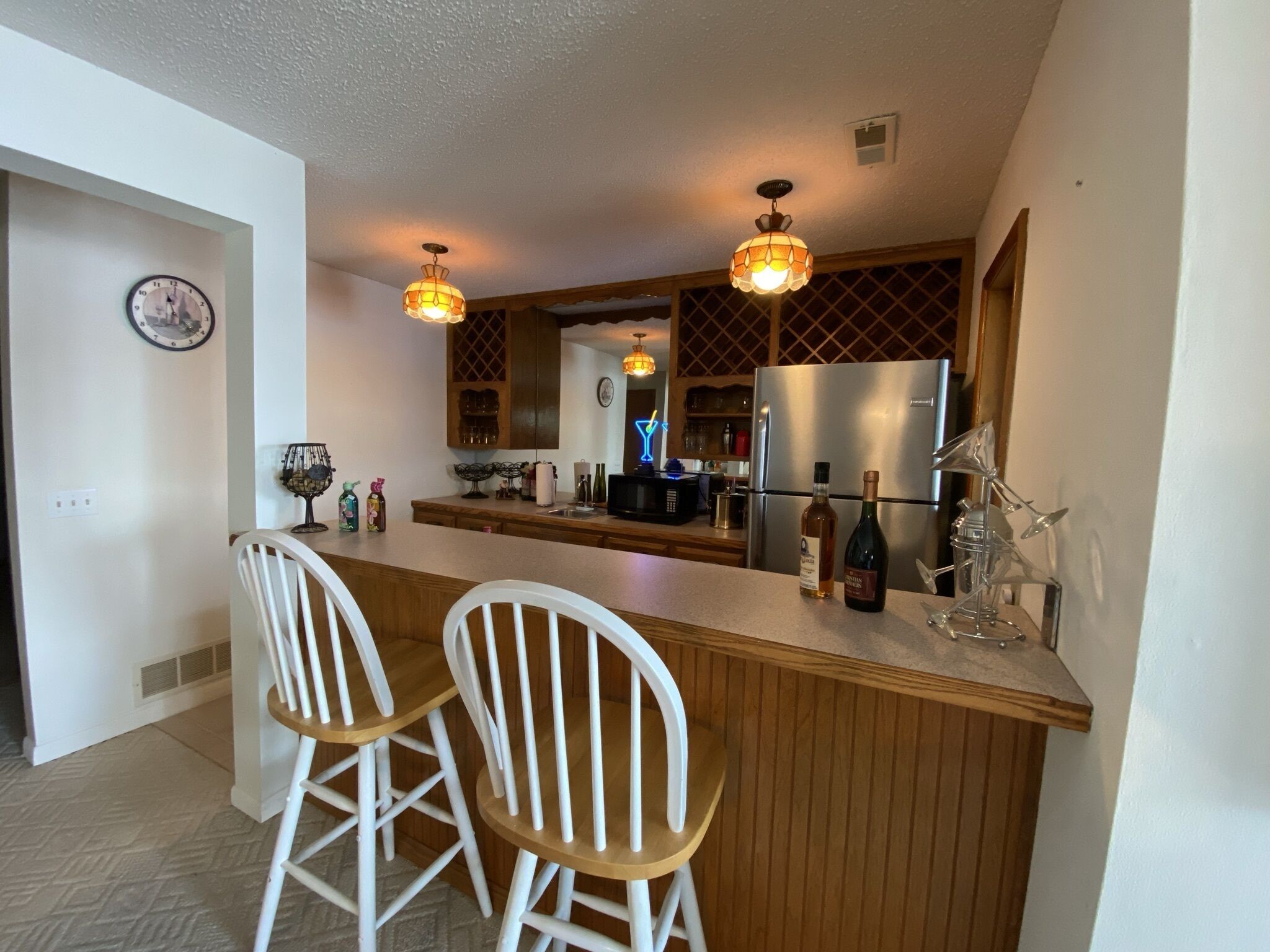 A modern kitchen with a central island, bar stools, pendant lighting, and a refrigerator.