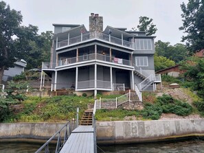 A multi-story house with a balcony and a dock leading to a body of water.