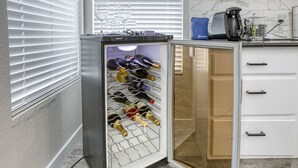 A compact wine refrigerator with a wine rack, situated in a kitchen with white cabinetry and a tiled backsplash. - Modern, Fully Renovated 4 Bedroom House (Las Vegas)
