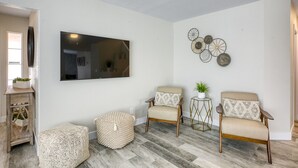 A living room with a flat-screen TV, two armchairs, a round ottoman, and a small side table with a plant. - Modern, Fully Renovated 4 Bedroom House (Las Vegas)