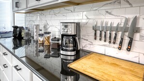 A modern kitchen with white cabinets, a marble backsplash, a coffee maker, and a knife rack. - Modern, Fully Renovated 4 Bedroom House (Las Vegas)