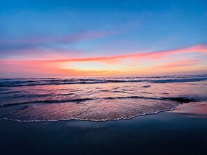 A beach at sunset with waves approaching the shore.