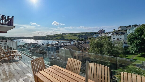 A wooden deck with a table and chairs overlooking a coastal town with buildings and boats.