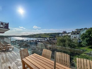 En træterrasse med et bord og stole med udsigt over en kystby med bygninger og både.