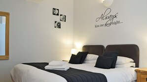 A neatly made bed with a black and white striped bedspread, a wall with a floral artwork, and a wall-mounted light fixture. - Caddys Cottage - UK6714 (Lydstep, near Tenby)