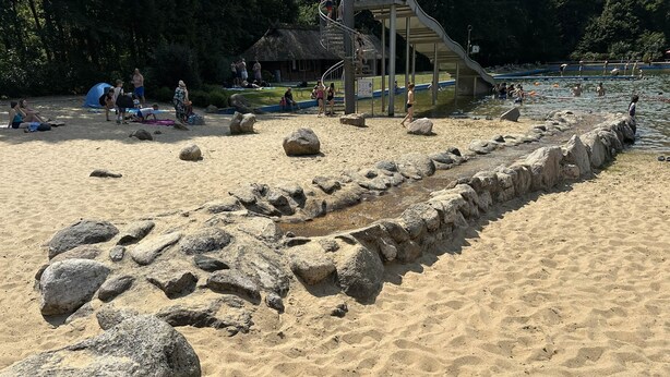 Una playa arenosa con rocas grandes y un muro de piedra.