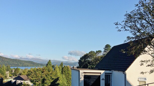 Un edificio blanco con puerta de garaje, rodeado de vegetación y con vista a montañas.