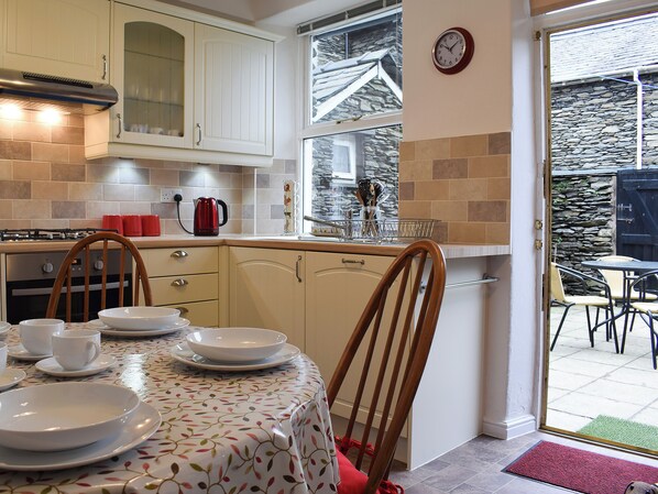 A kitchen with a dining area, featuring a stove, cabinets, and a dining table set with plates and cups. - 2 bedroom accommodation in Windermere (Windermere)