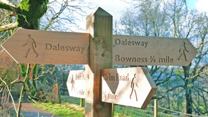 Un cartel de madera señala con flechas Dalesway, Bowness y Helm Road, indicando una distancia de 1/4 de milla para cada uno.