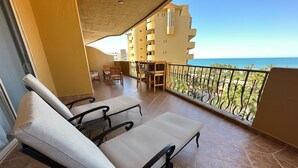Un balcón con dos sillones de descanso, una mesa y sillas, con vistas a un edificio y al mar.