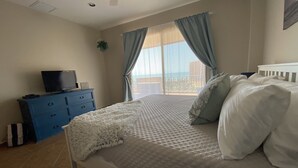 Un dormitorio con cama, cómoda, televisor y ventana con cortinas.