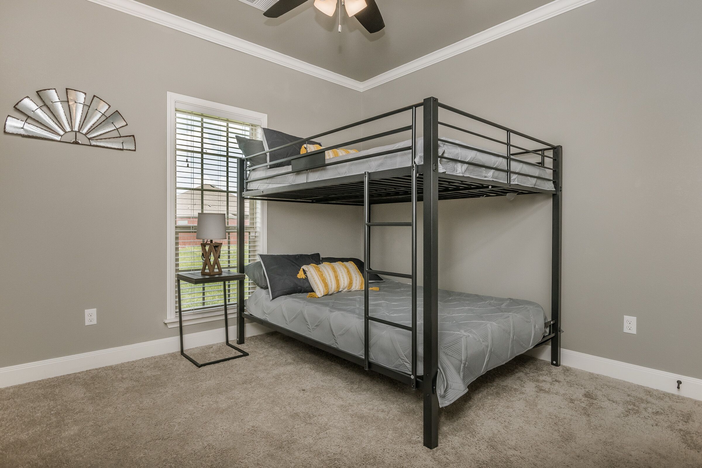 A bunk bed room with a ceiling fan, a window with blinds, and a decorative wall piece.