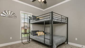 A bunk bed room with a ceiling fan, a window with blinds, and a decorative wall piece.