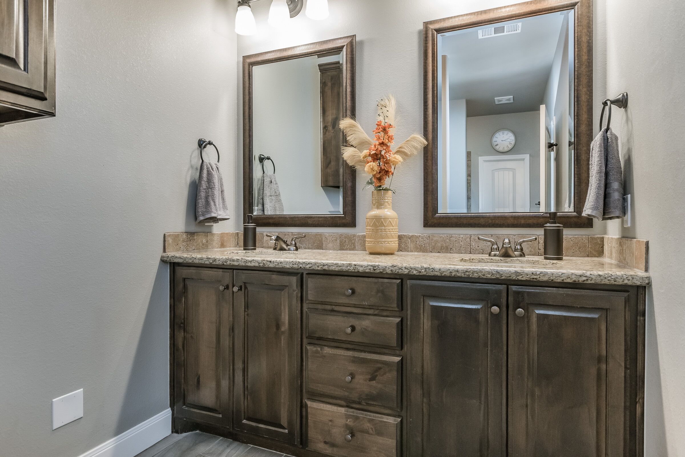 A bathroom with a dark wood vanity, a large mirror, and a vase with flowers.