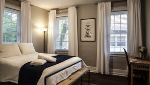 Un dormitorio con una cama, una mesita de noche con lámpara y una ventana con cortinas.