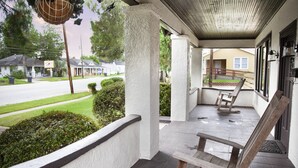 Un porche cubierto con un banco, una lámpara colgante y vista a una calle residencial.