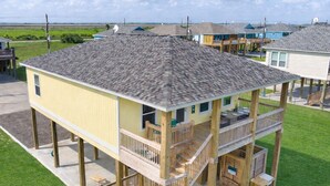 A two-story wooden house with a balcony, a deck, and a small outdoor seating area. - Beach Bungalow With Private Hot Tub (Bolivar Peninsula)