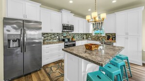 A kitchen with white cabinets, stainless steel appliances, a granite countertop, and teal bar stools. - Beach Bungalow With Private Hot Tub (Bolivar Peninsula)