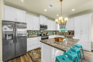 A kitchen with white cabinets, stainless steel appliances, a granite countertop, and teal bar stools.