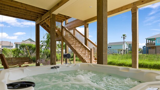 A hot tub with a wooden deck and stairs, surrounded by greenery and houses. - Beach Bungalow With Private Hot Tub (Bolivar Peninsula)