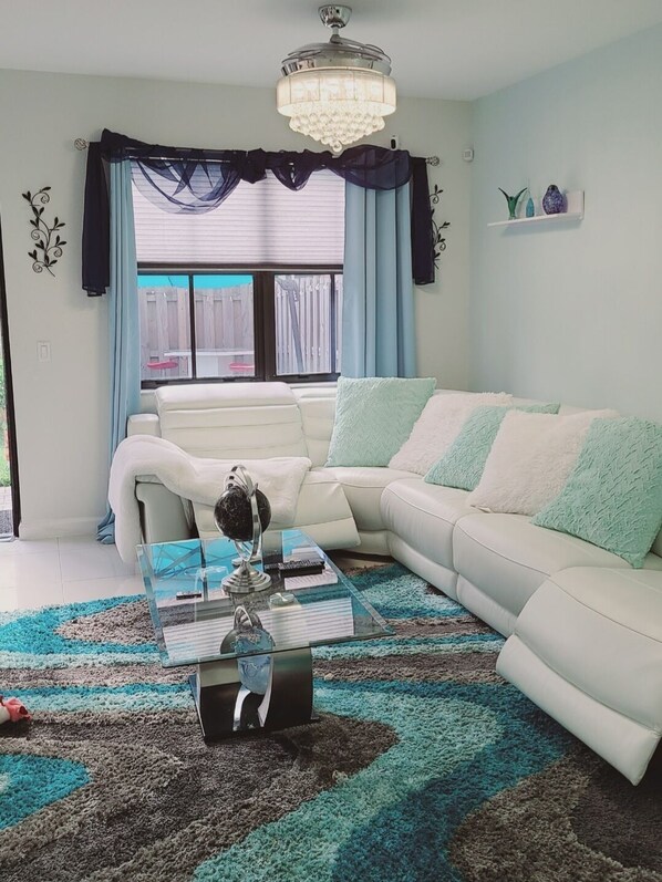 A living room with a white sofa, a glass coffee table, and a chandelier.