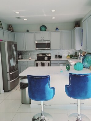 A modern kitchen with light grey cabinets, stainless steel appliances, and a central island with two blue bar stools.