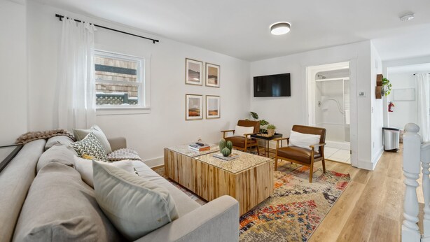 A modern living room with a sofa, coffee table, and chairs. There is a TV mounted on the wall and a window with curtains. - Welcome to The Palms! Your summer retreat ~Hot tub (Fort Erie)