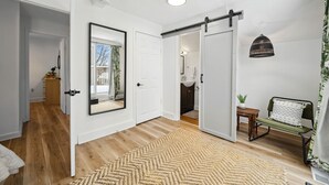 A modern interior with a sliding door leading to a bathroom, a wooden floor, and a large mirror. - Welcome to The Palms! Your summer retreat ~Hot tub (Fort Erie)