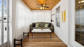 A cozy room with a wooden ceiling, a green sofa with cushions, a white coffee table, and a window with yellow curtains. - Welcome to The Palms! Your summer retreat ~Hot tub (Fort Erie)