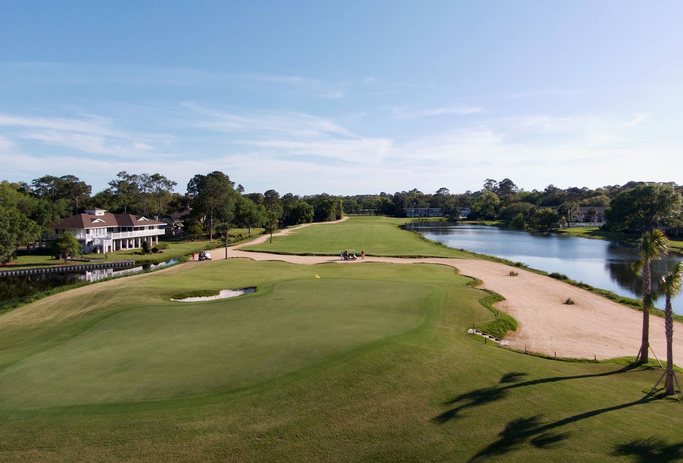 A golf course with a water body, a clubhouse, and a sandy area.