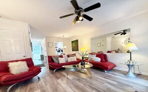 A living room with red leather sofas, a glass coffee table, a ceiling fan, and a dining table with a lamp.