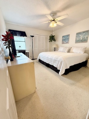 A bedroom with a bed, a desk, a ceiling fan, a window with curtains, and a wall-mounted plant.