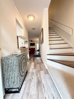 A hallway with a staircase, wooden flooring, and a patterned console table.