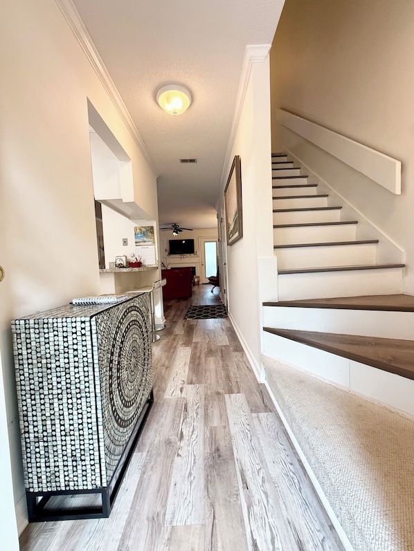 A hallway with a staircase, wooden flooring, and a patterned console table. - Spacious townhouse with lots of amenities not far from the beach. (St. Simons Island)