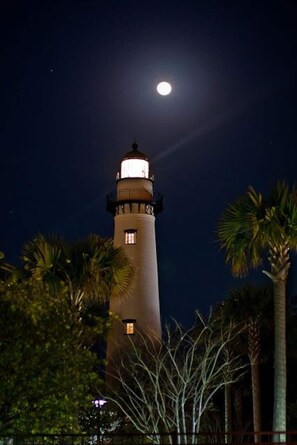 Un faro alto y cilíndrico con una luz en la parte superior, rodeado de palmeras.